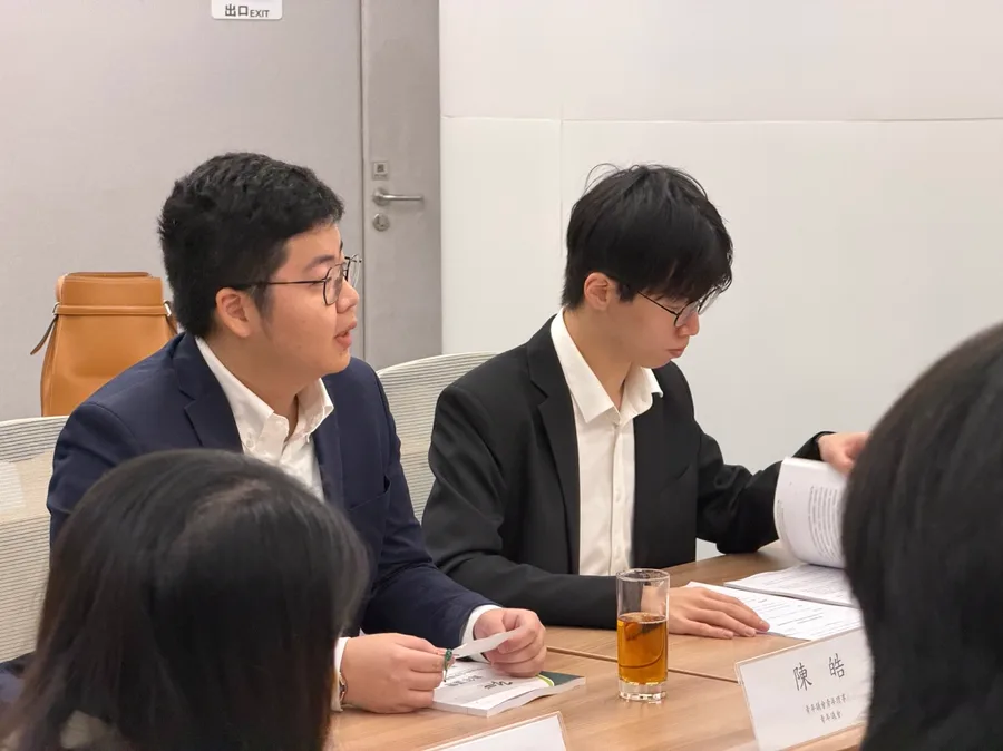 兩位男學員在會議桌前發言，桌上放有建議書文件與座位名牌。